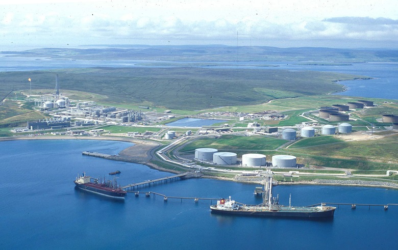 An aerial photo of two large ships docked at an oil terminal. The Shetland Isles can be seen stretching out in the distance,