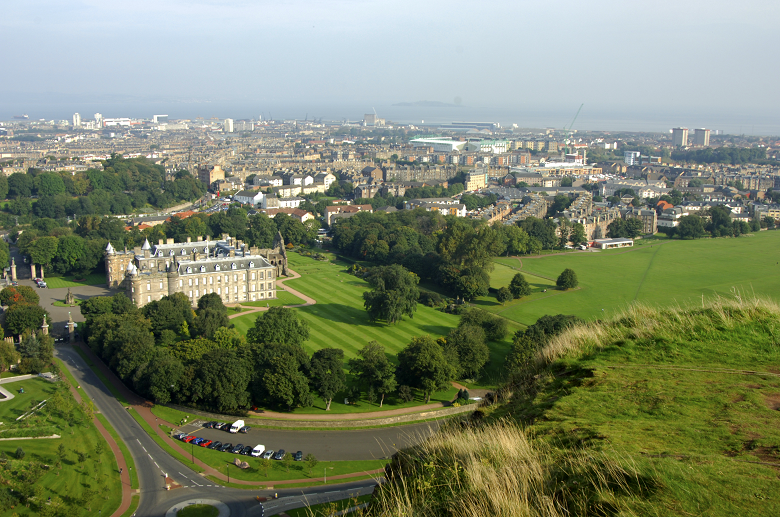 A palace on the fringes of a large park with the city of Edinburgh in the background