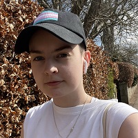 a young person with short hair wearing a black cap with the trans pride flag on it.