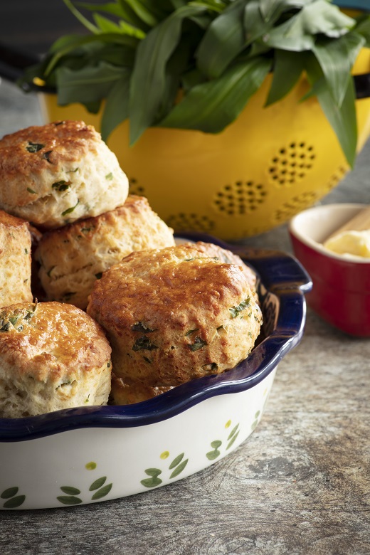 A bowl of scones with a smaller bowl of butter and some wild garlic in the background