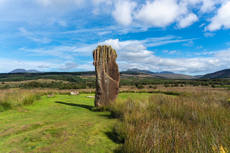 A standing stone on Machrie Moor, a heath with rolling hills behind.