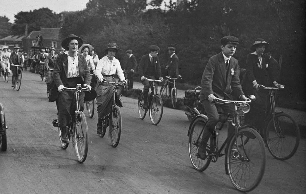A black and white archive photo of a cycling rally in 1910. There are men and women in the group and a range of ages.