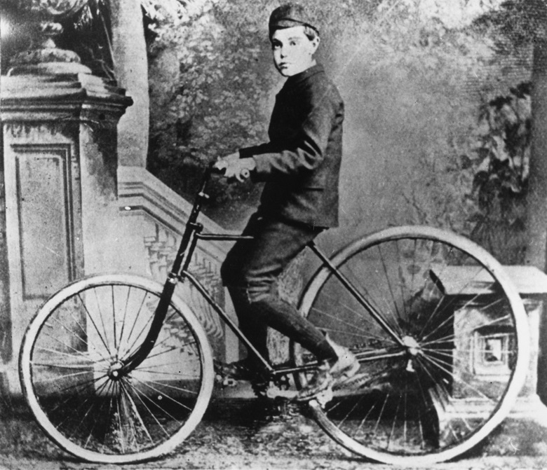 A black and white archive photo of a boy, aged around 10, on a bicycle with pneumatic tyres 