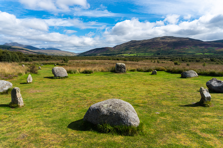 A stone circle consisting of smaller stones of different shapes in a dramtic, ioslated location on a moor, with mountains rising in the background