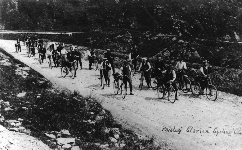 An archive photo of a large group of cyclists making their way down a country road. Most of them are walking alongside their machine! 