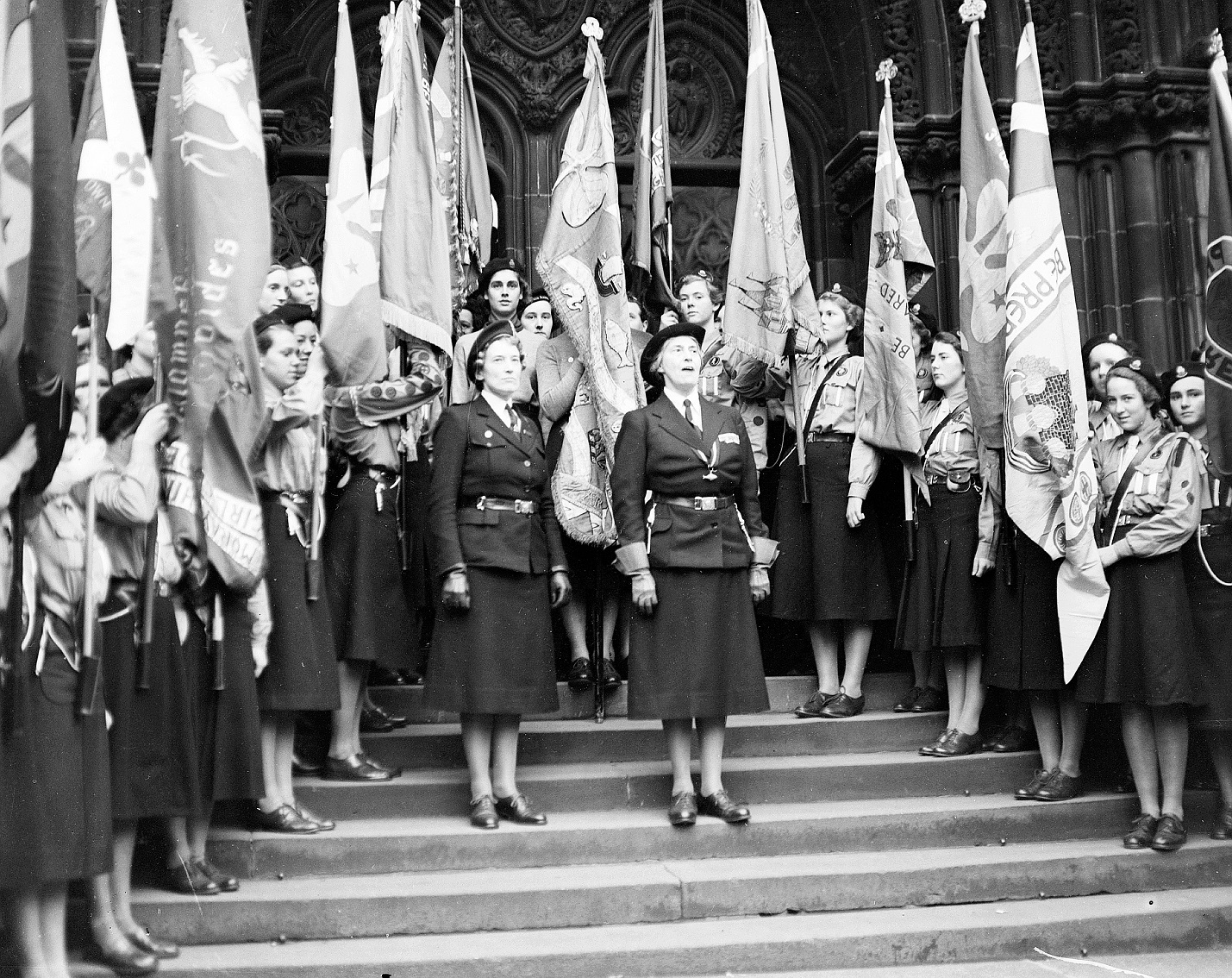 A black and white archive photo of the Scottish Girl Guides at St Giles Service. Lady Baden-Powell is addressing the room from the steps at the West Door.