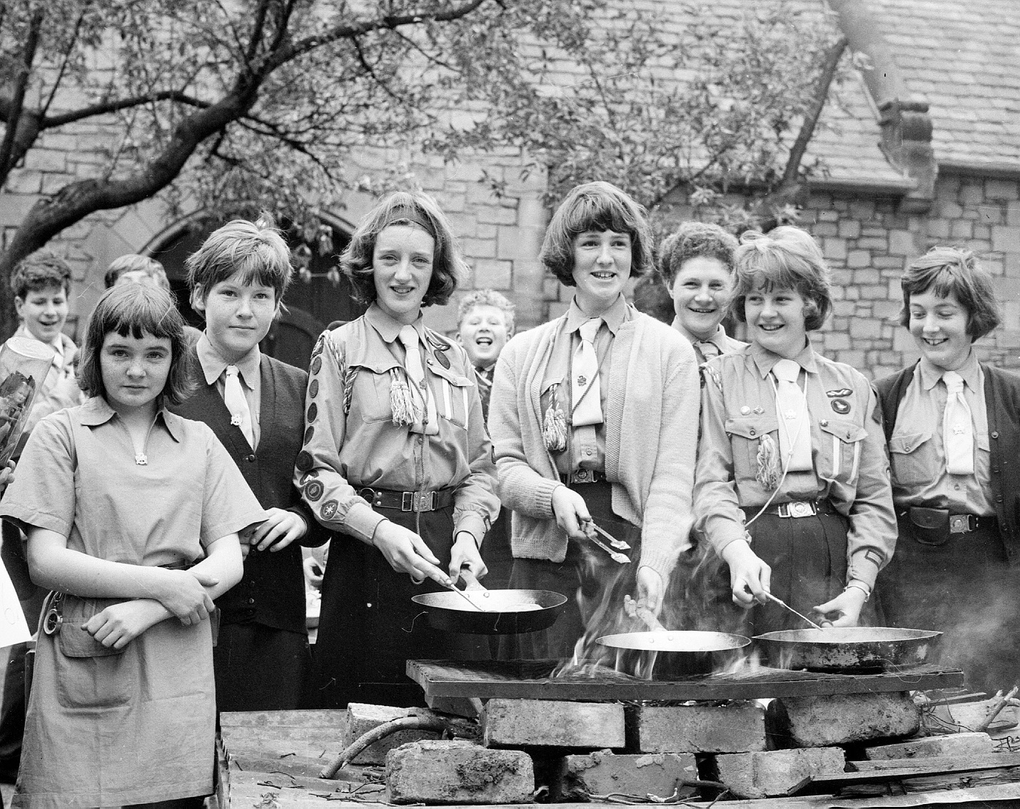 A black and white photo of a girlguiding group of women and girls stirring pots at a barbeque.