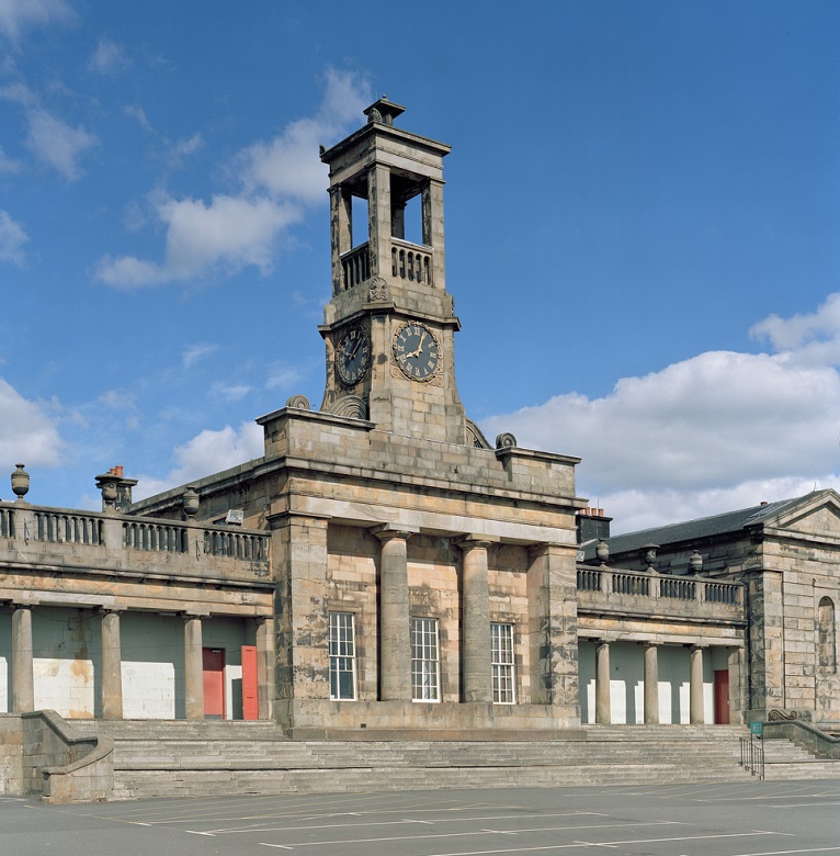 A grand former school building. The building has a columned facade and is topped by a small but ornate clock tower.