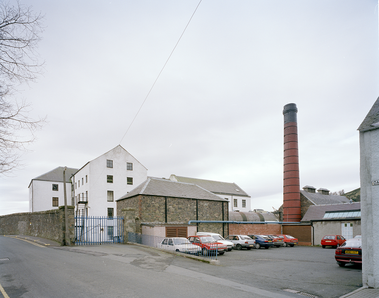 An archive photo of a mill building focusing on a rectangular brick boiler house and a large, red chimney. 
