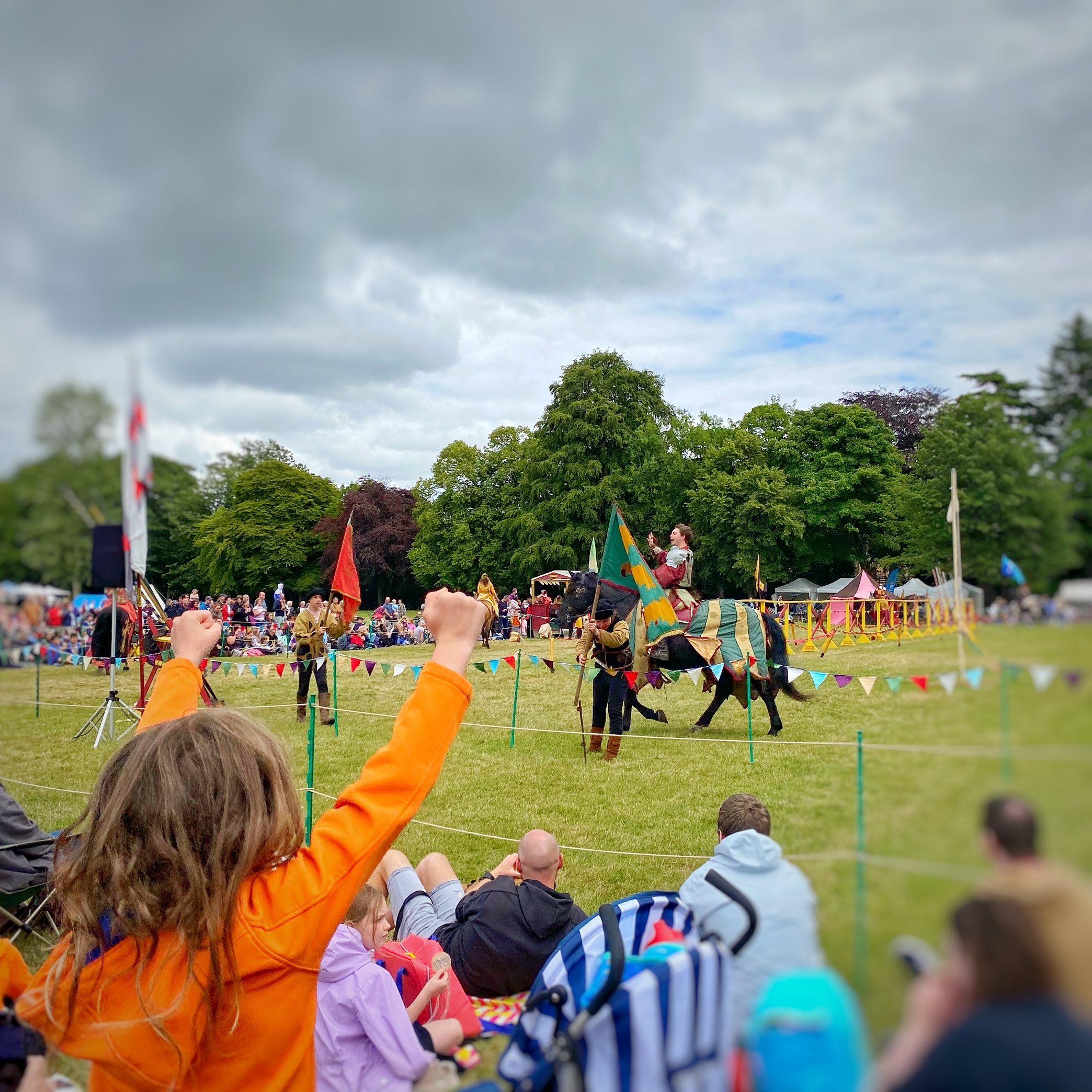 Photo taken at a jousting tournament at Linlithgow Palace. You can see a cheering child in the crowd with their back to the camera watching the tournament.