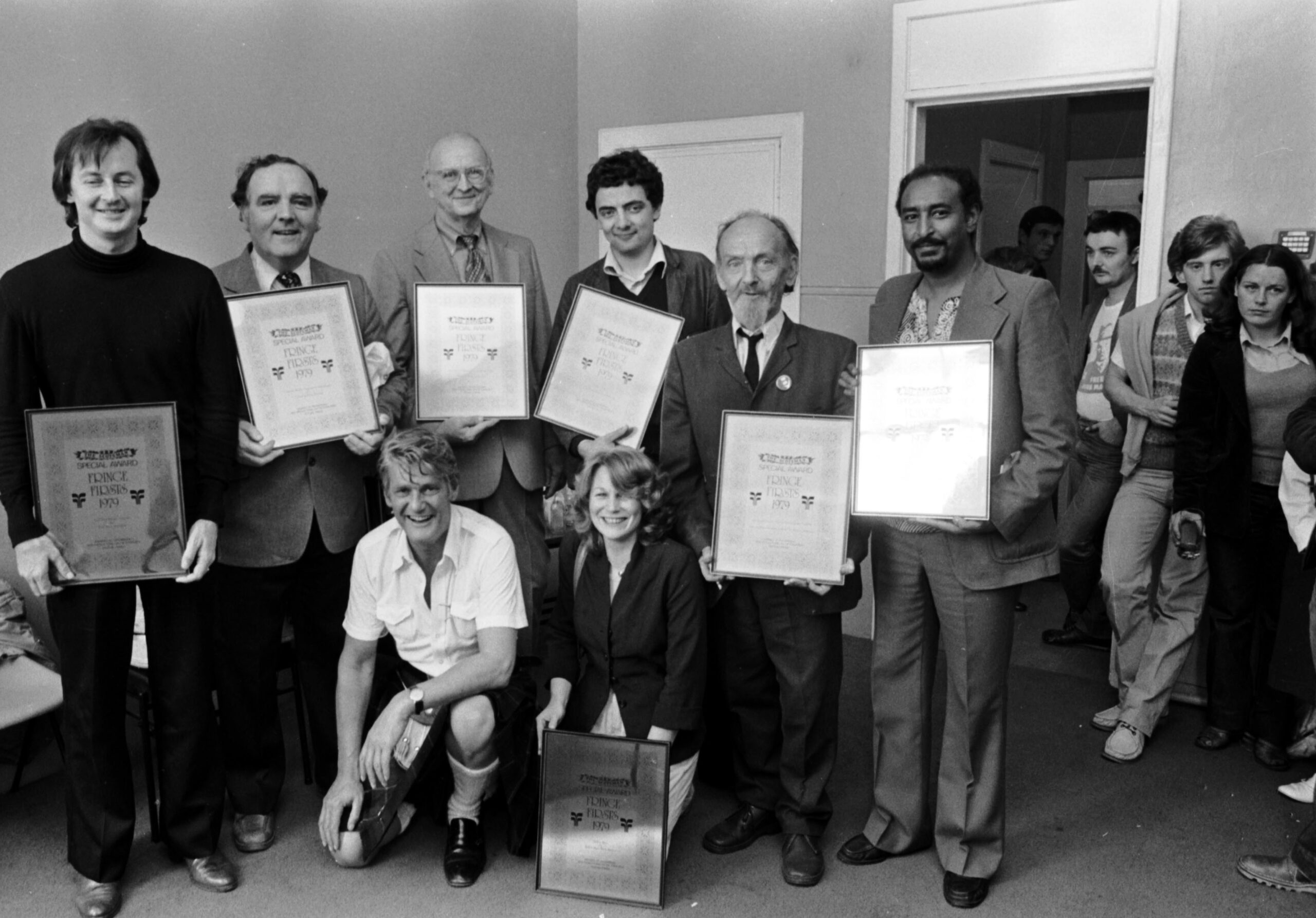 A black and white archive photo of the recipients of the Fringe First awards. A young Rowan Atkinson is in the middle smiling at the camera. 