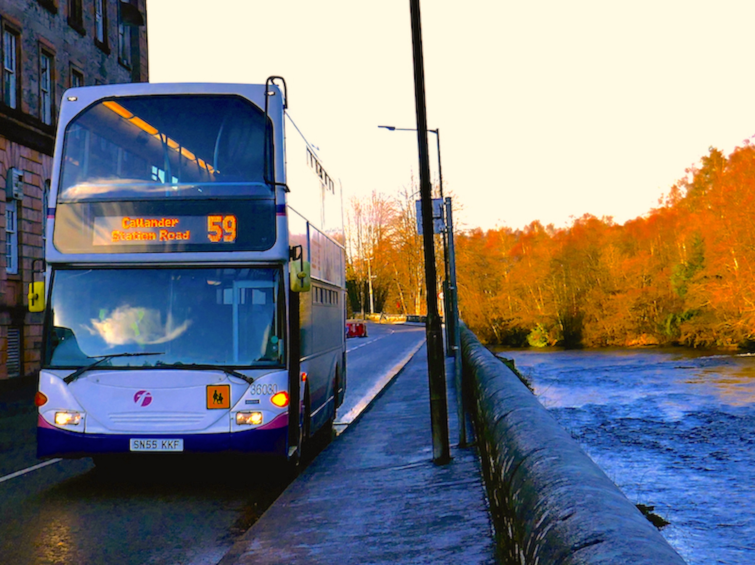 A double decker bus with the number 59 on it on the side of a road next to a river