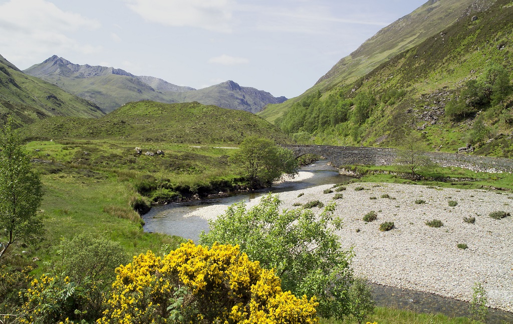 A stone bridge crossing a river running through a secluded and beautiful Scottish glen