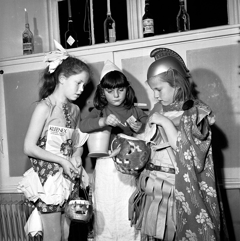 Three wee girls in fancy dress lighting their turnip lantern.