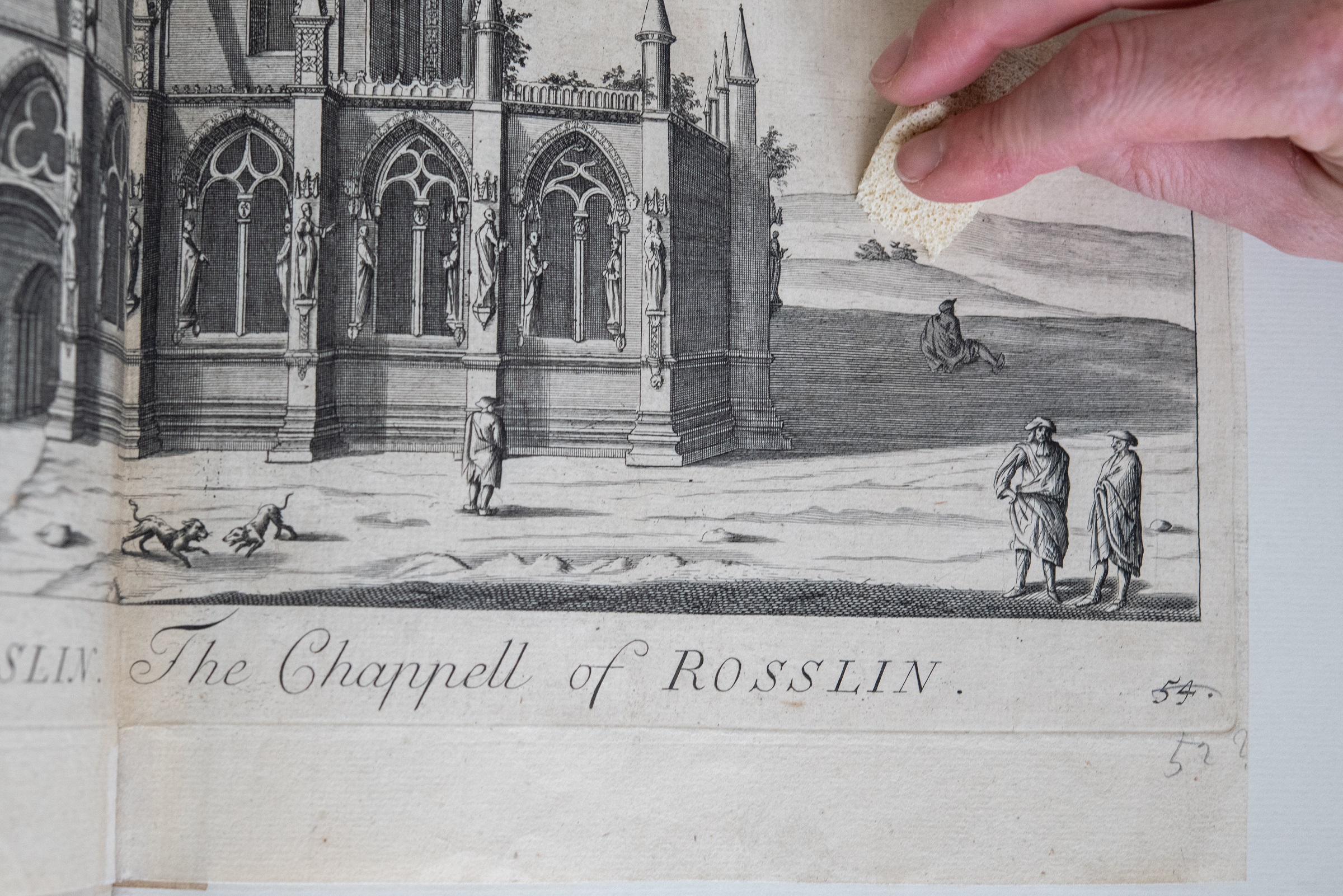 A close up showing a page of the book. A hand is shown cleaning the page with a small sponge. 