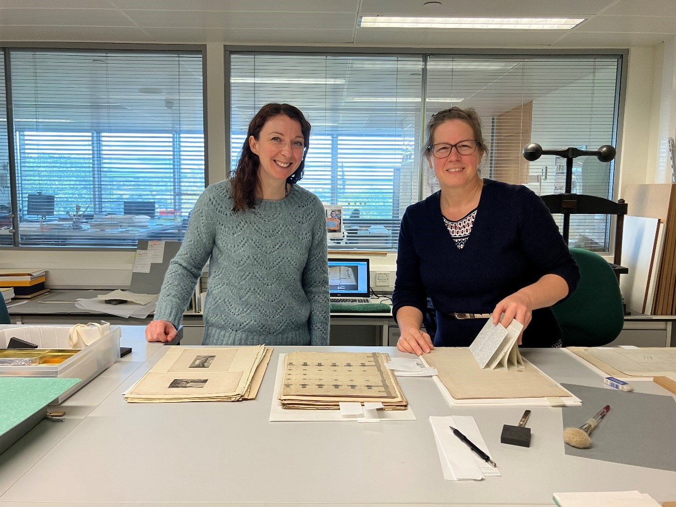 Two women smiling at the camera while working on the manuscript