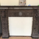 An ornately carved stone fireplace which has been boarded up.
