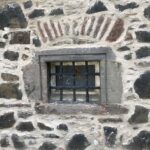 A very small window in a stone wall covered by old-looking metal bars