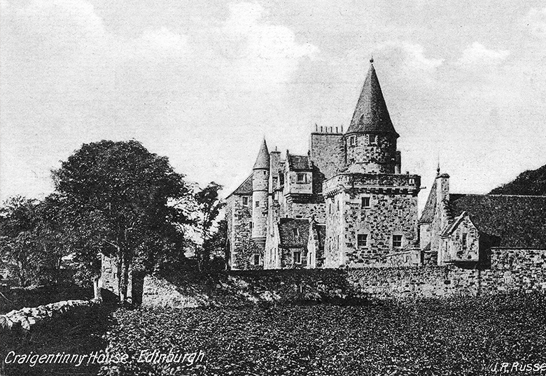 A black and white postcard of an impressive tower house with various turrets behind a large estate wall.
