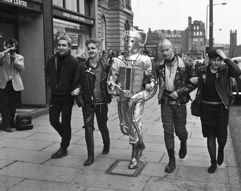A black and white archive photo showing punks arm in arm with a Cyberman walking down Lothian Road in Edinburgh