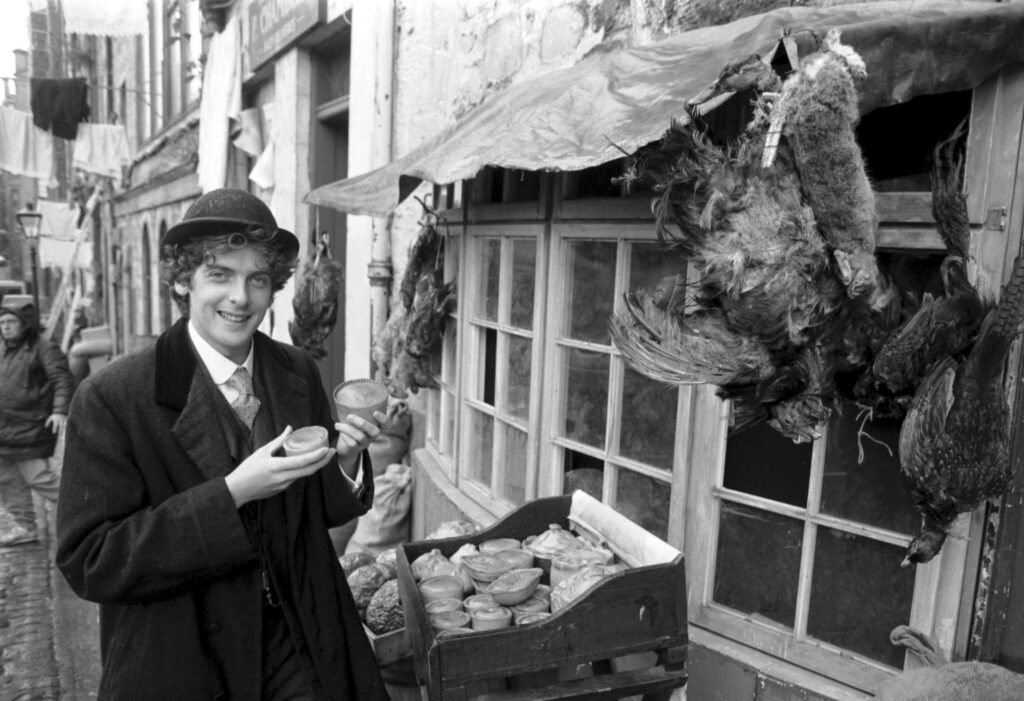 A black and white archive photo showing Scottish actor Peter Capaldi outside a pie and game shop in Niddry Street Edinburgh.