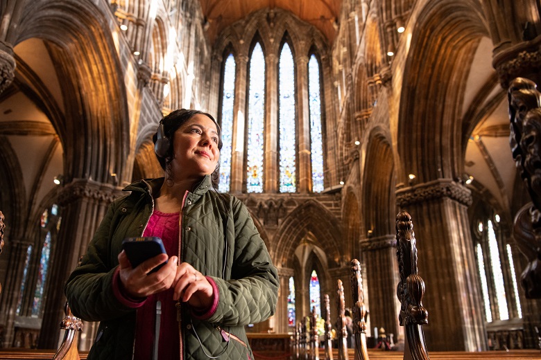 A visitor to Glasgow Cathedral listening to an audio guide using their mobile phone and headphones 