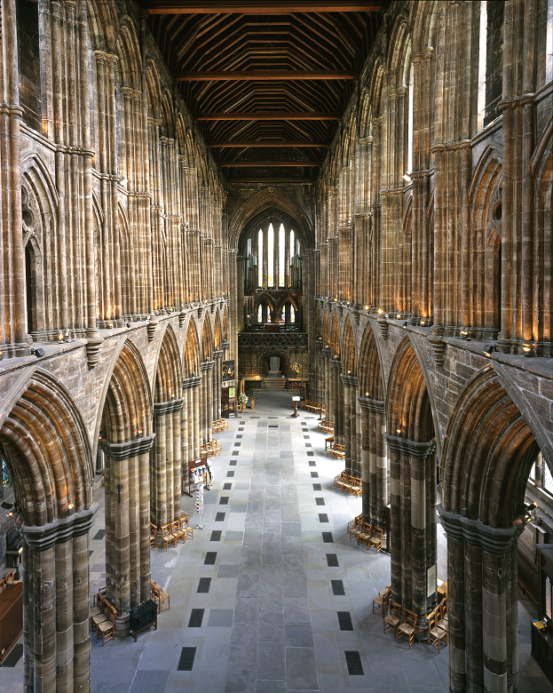 A photo taken from a gallery above the nave of Glasgow Cathedral. It shows the enormous space which is dominated by stone arches and columns. A wide aisle leads to the distant altar and choir. 