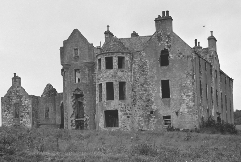 Black and white archive photo of a derelict castle. It's a large 3-storey building in very bad disrepair. ALl of the wondows have gone, some walls are crumbling and the roof is losing slates.