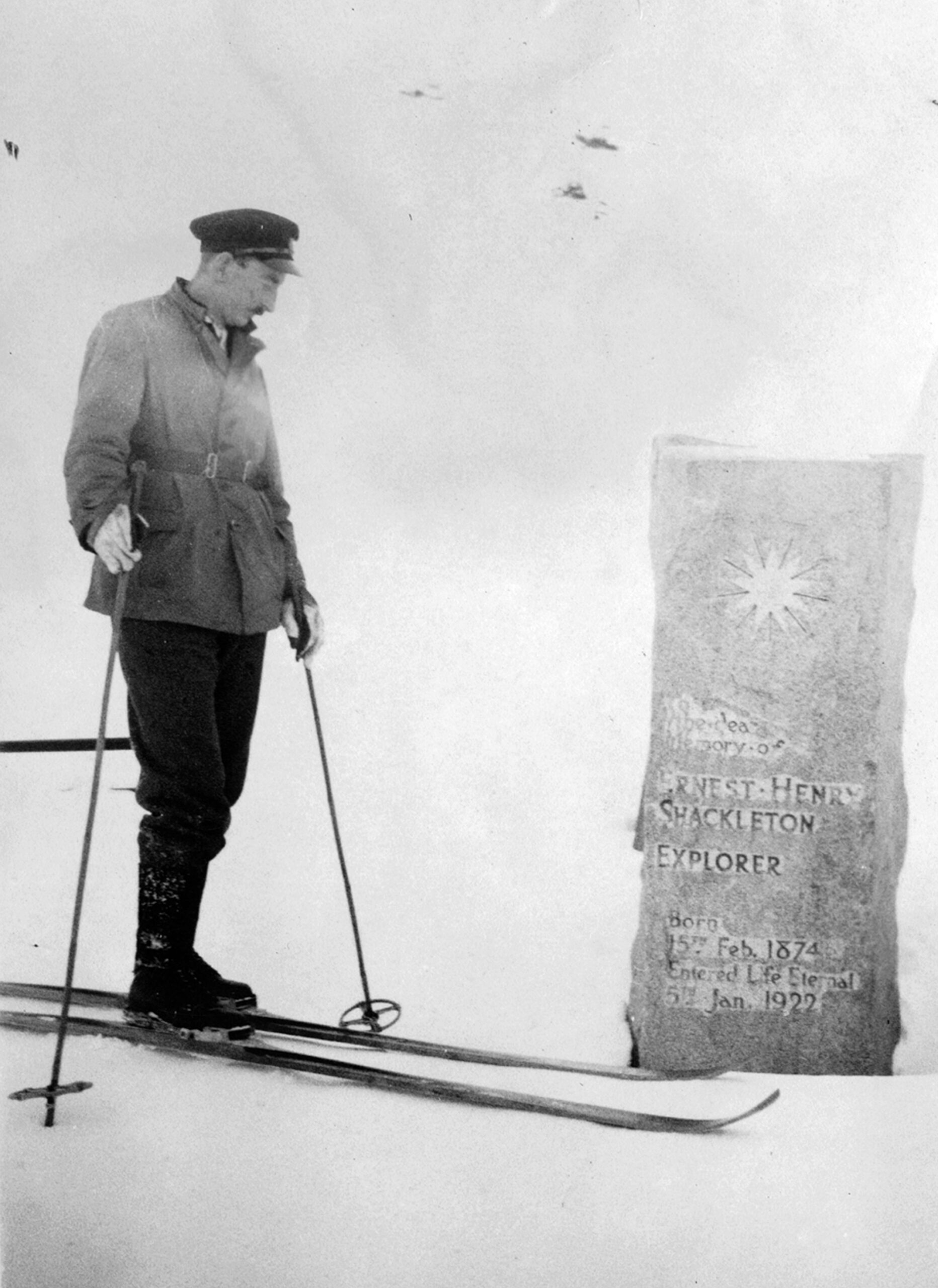 A black and white archive photo showing a grave and a man on skiers next to it.