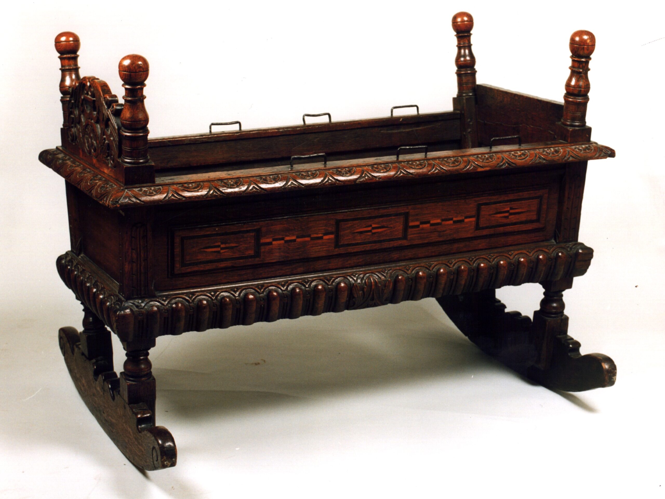 A dark wooden cradle with ornate decorations on rockers.