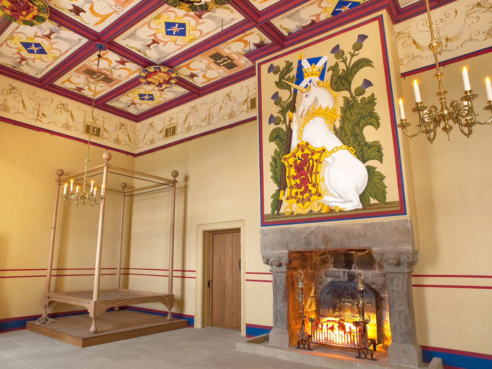 A reconstruction drawing showing a rich room hung with tapestries and with a paneled ceiling. There is a four-poster bed in the corner. A large fireplace with a long table in front of it.