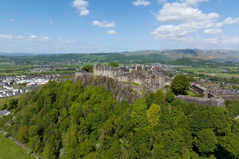 A drone image of Stirling Castle sitting on top of a large crag covered with trees.