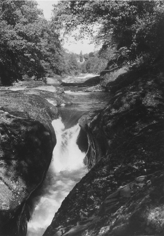A black and white archive photo showing a narrow, rocky section of a tree-lined river.