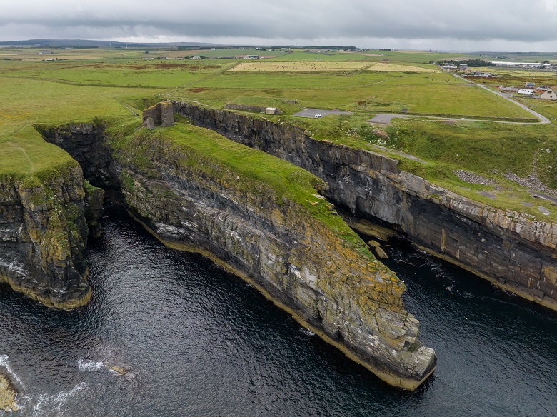 A photo taken by drone of a ruined castle dramatically situated on the edge of steep, rocky cliffs. Only the tower of the castle has survived intact. 