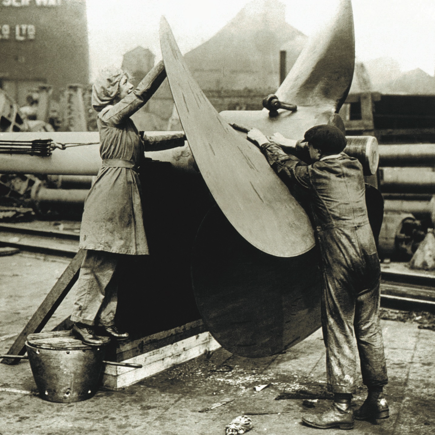A black and white archive photo showing two women working on a large ship part.