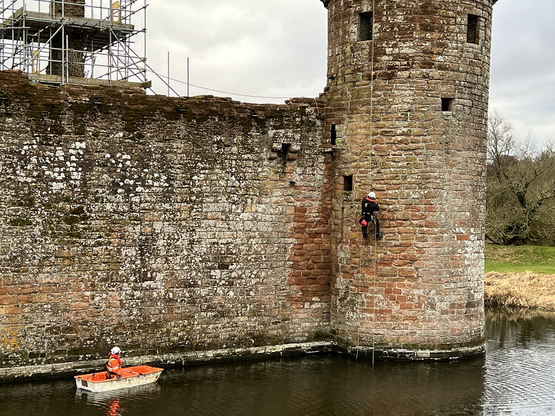 A team inspecting the exterior wall of a castle. Because of the castle moat, they have has to use a small boat to gain access.