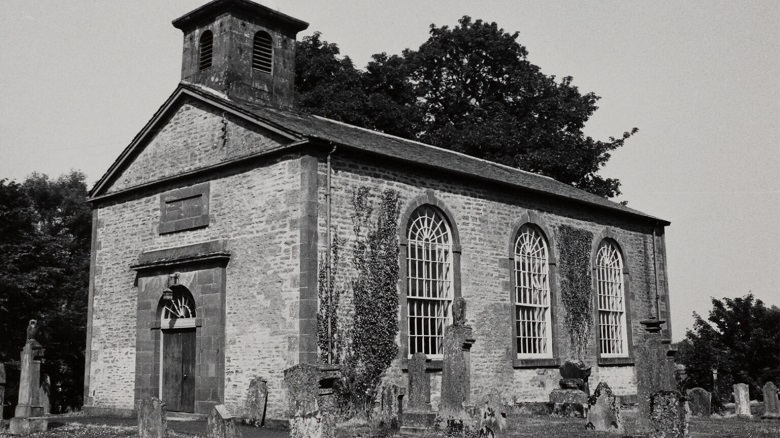 A black and white archive photo of a modest church building surrounded by gravestones
