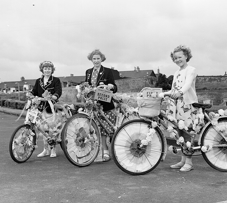 Three secondary school aged girls posing with bikes which have been decorated with flowers and coloured paper for a gala day 