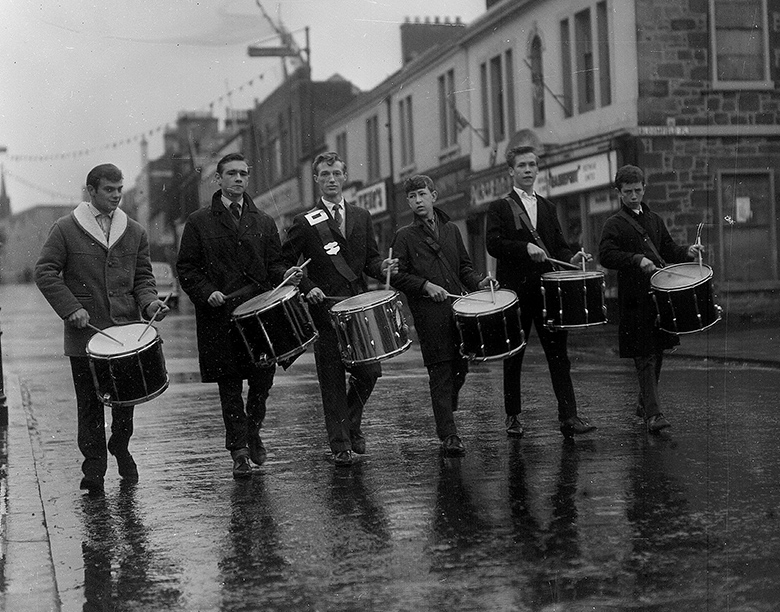 An archive photo of six drummers walking down a town street 