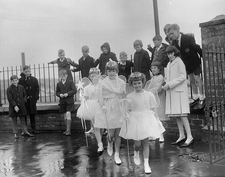 A crowd of young onlookers watch as three girls dressed as fairies pose for the camera on what looks to be a rather wet gala day.