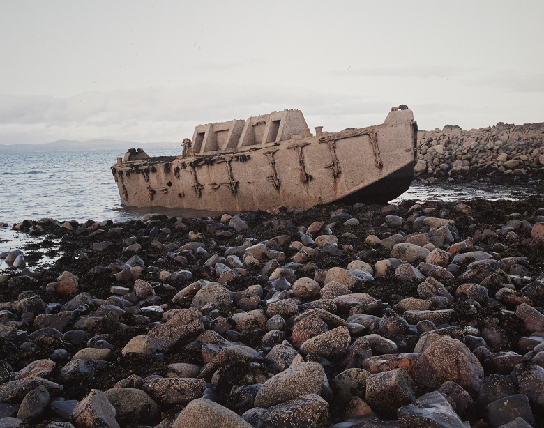 A large concrete structure which was part of a temporary harbour structure. It has been washed up on a rocky beach and now lies abandoned 