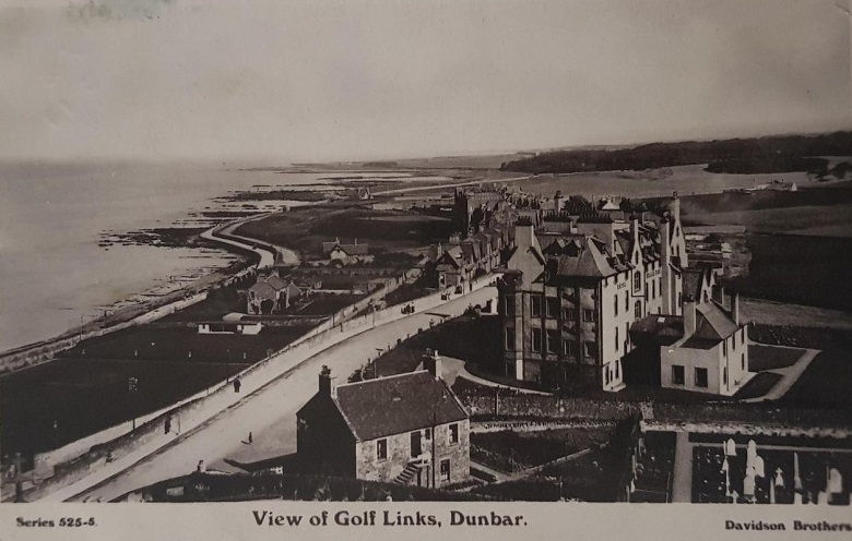 A black and white postcard showing a large hotel overlooking a town and its beach