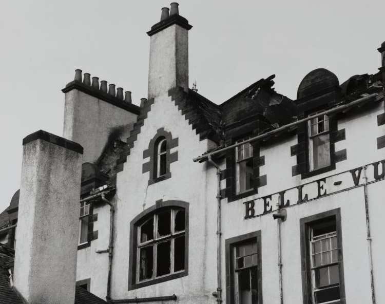 A close-up photo of part of the Belle-Vue hotel in a derelict state with part of the roof missing. Large black letter spelling out the hotel's name still adorns the walls. 