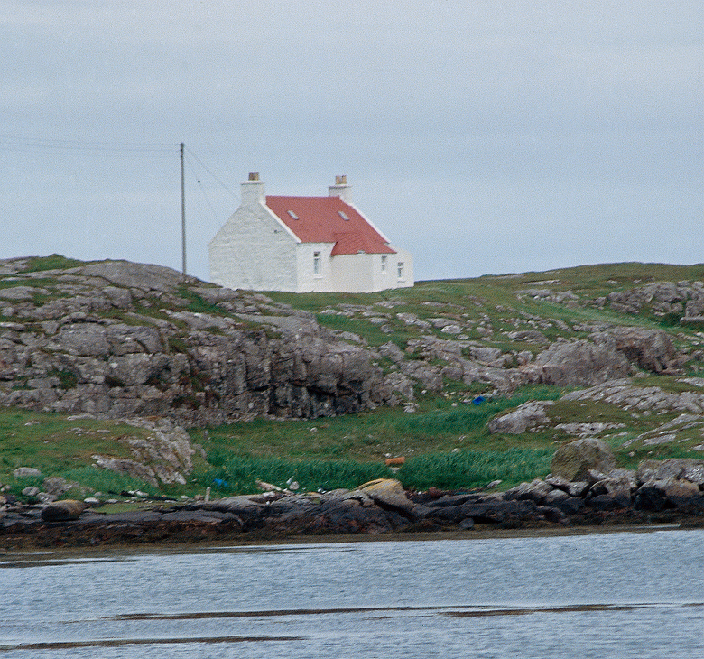 A small whitewashed house or croft beside the sea. It has a red roof. 