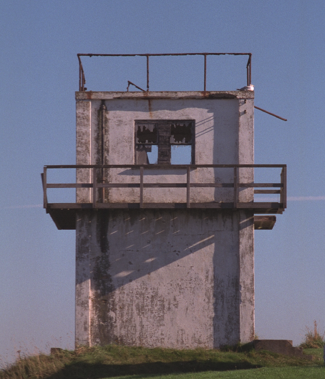 A squat lookout tower made from whitewashed concrete with a metal balcony.
