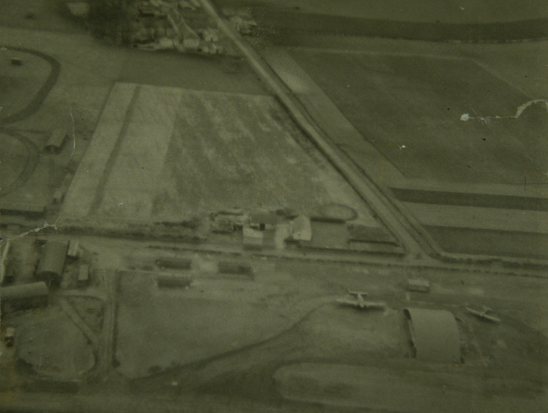 An archive aerial photo showing a basic grass airfield surrounded by farmland. Hangers and a number of aircraft can be made out. 