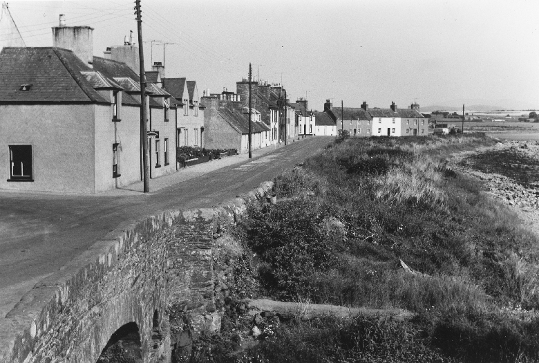 A black and white archive image of a small coastal village with a row of cottages facing a sandy beach