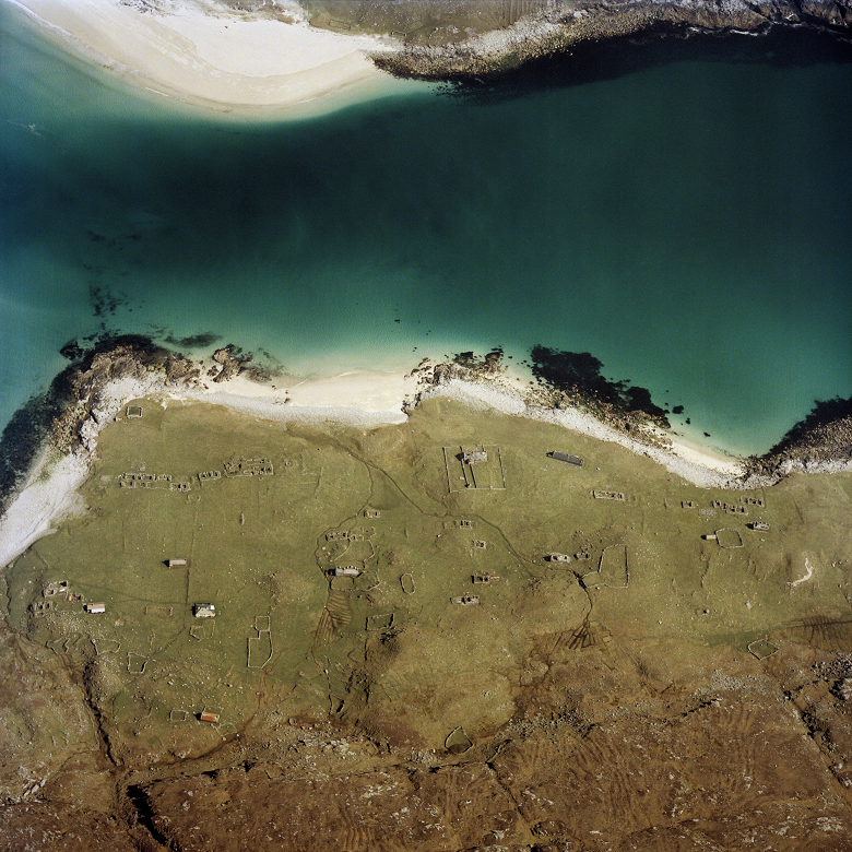 An aerial photo of a short expanse of bright turquoise sea between two Hebridean islands. Both have idyllic sandy beaches. The remains of deserted crofts can be made out in the fields. 