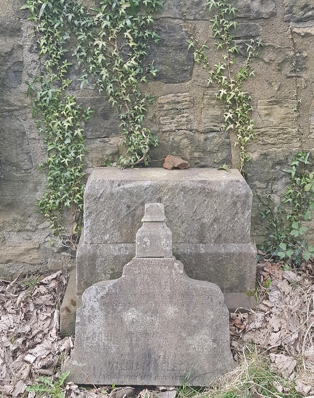 A gravestone in a rather ruinous state. The top of the stone appears to have fallen or been removed from its base. The name William Fleck can be made out. 