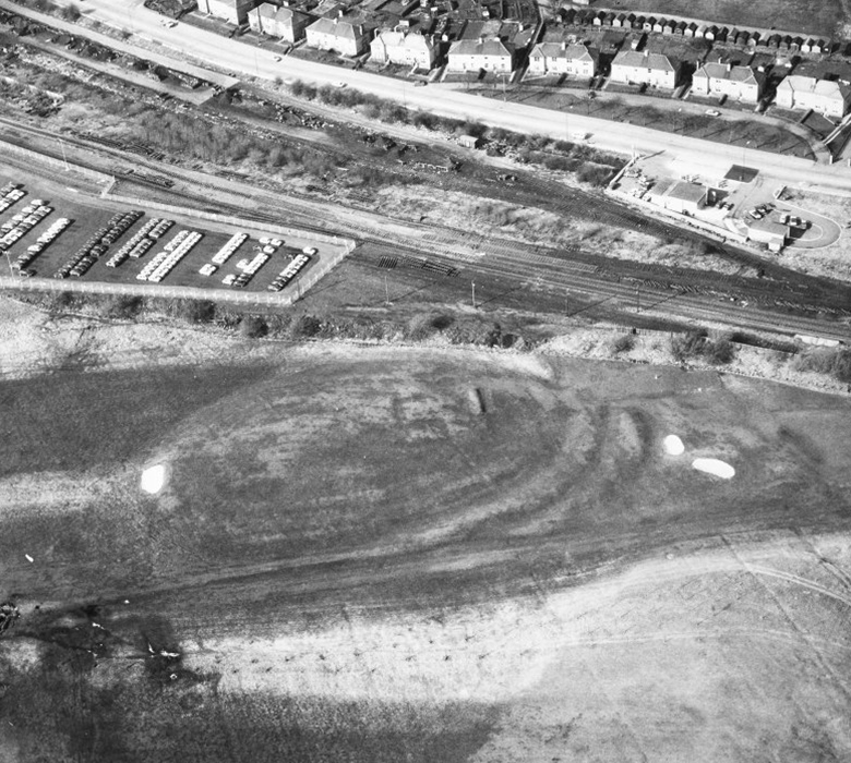 An aerial image which shows circular earthworks of a fort in the grass of a golf course.